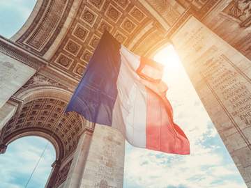 french flag flying underneath the arc de triomphe