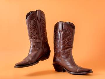 two elegant classic cowboy boots on an orange clay background