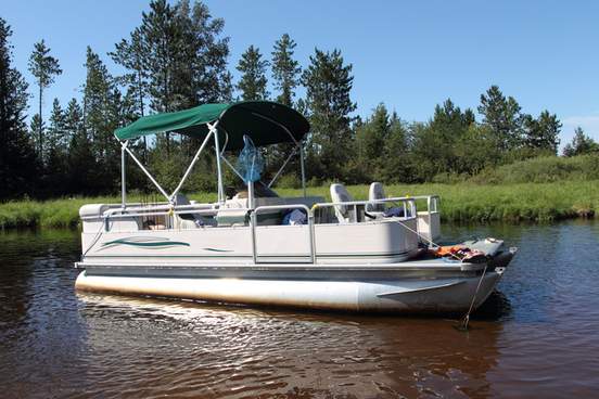 a big pontoon boat anchored in the river with fishing poles and the canopy up