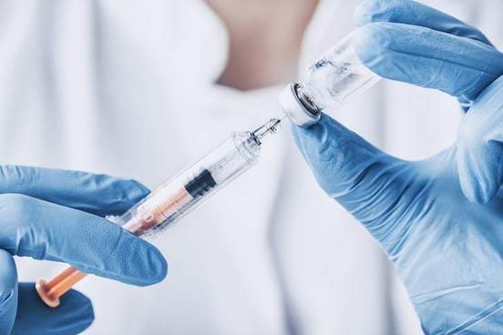 a doctor wearing medical gloves filling up a syringe with a vaccination