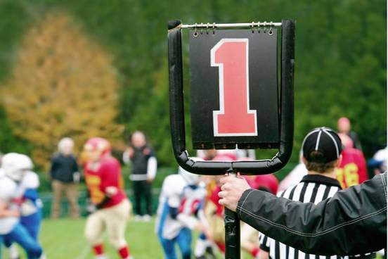 american footbal men are looking at field while signpost shows number one indicating that this is a first down play