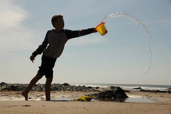 boy throwing bucket of water on beach