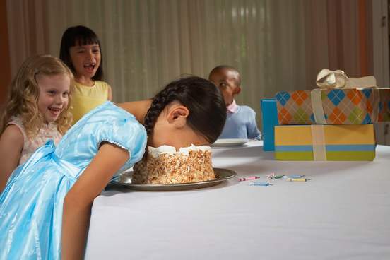 children laughing at girl who has her face in a cake