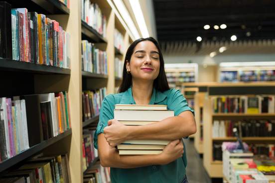 excited woman looking happy carrying a lot of books while buying novels at the bookstore