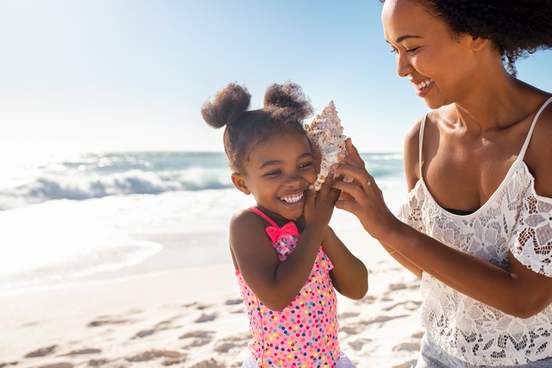 girl listens to a seashell at the beach