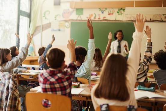 group of young students all raise their hands to answer a question