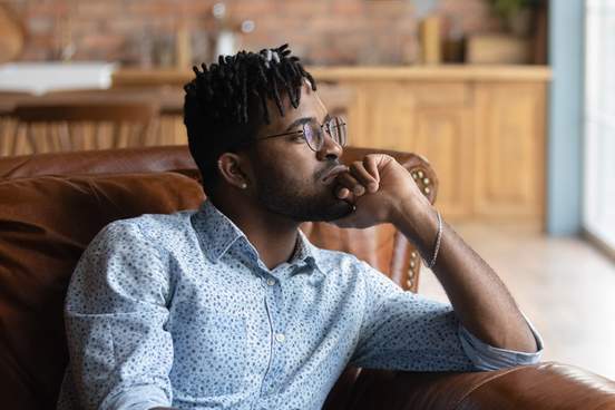 guy lost in thoughts sitting on coach looking away having a thought