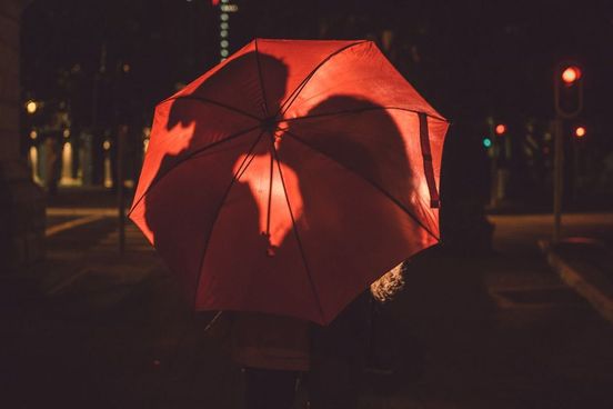 happy couple sharing kiss behind the red umbrella it is the same umbrella that appears in the stygian image a remembrance of a happier time