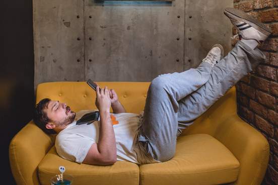 man lazes on sofa reading on his phone