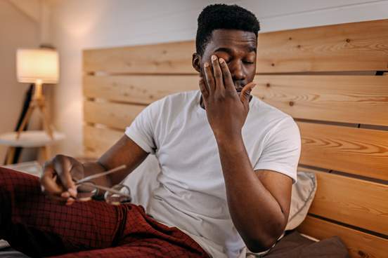 man rubbing his eyes in bed