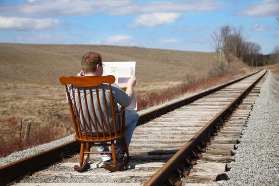 man sitting in chair on train tracks reading newspaper