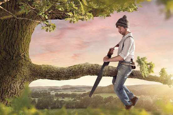 man sitting on branch cutting it with a saw