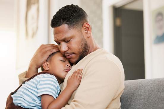 man tenderly holding his son who is asleep or sick
