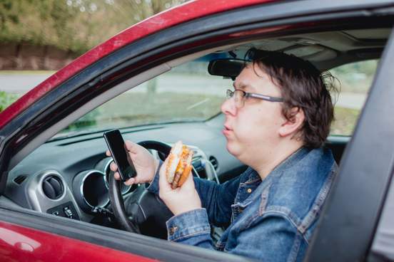 man wearing jean jacket eating hamburger inside his car