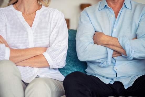 mature couple fighting at home sitting on the sofa they are both looking angry and have their arms crossed