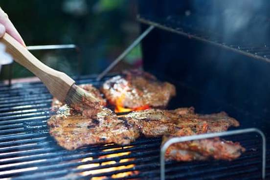 meat on barbecue being coated with marinade