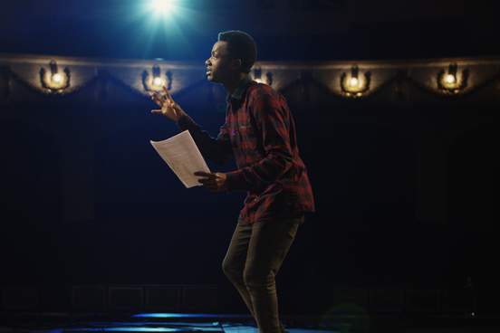 medium close-up shot of an actor performing a monologue in a theater while holding his script