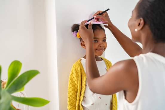 mother measuring daughters height on wall