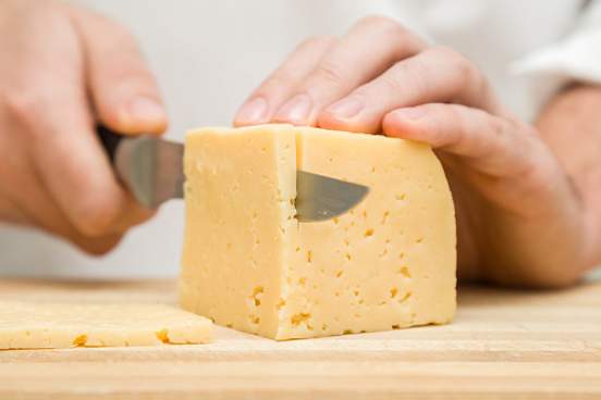 person cutting cheese with knife