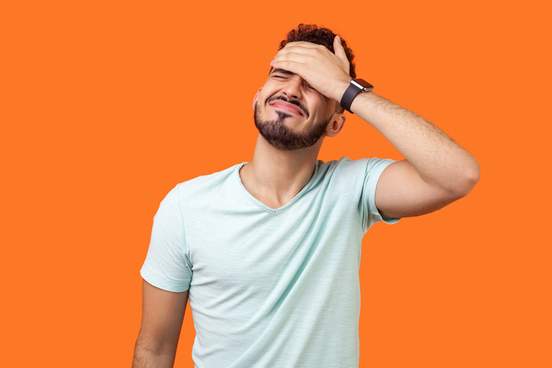 portrait of desperate brunette man with beard in white t-shirt covering face with hand feeling sorry and blaming himself for the mistake