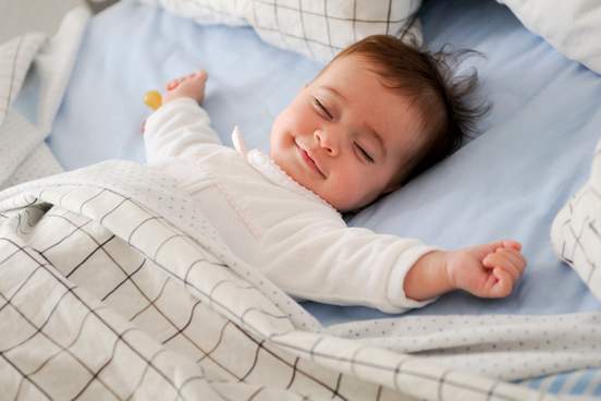 smiling baby girl lying on a bed sleeping and smiling on blue sheets