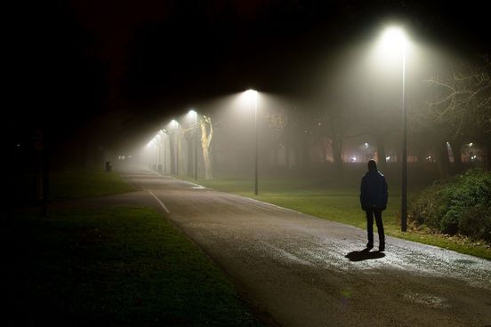 somber teen walks alone on a dark path the overhead floodlighting of streetlamps and the suburban setting hint at a deeper significance it is a metaphor maybe