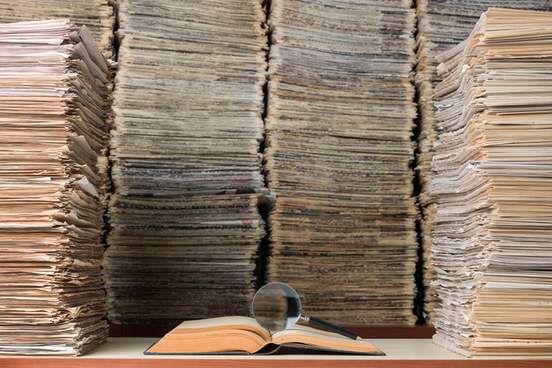 stack of newspapers and a single book with a magnifying glass in it