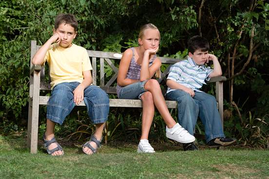 three bored and aimless children sit on a bench