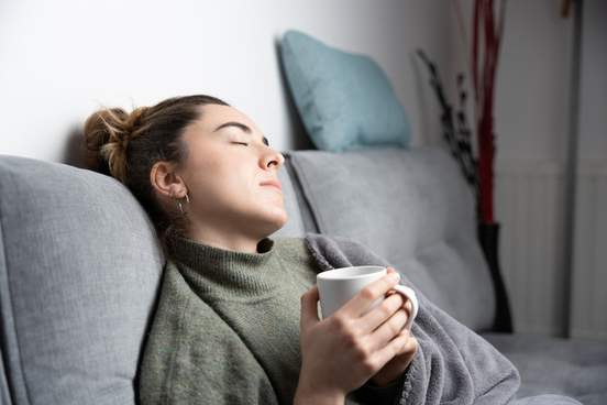tired woman resting on couch and holding a cup of tea
