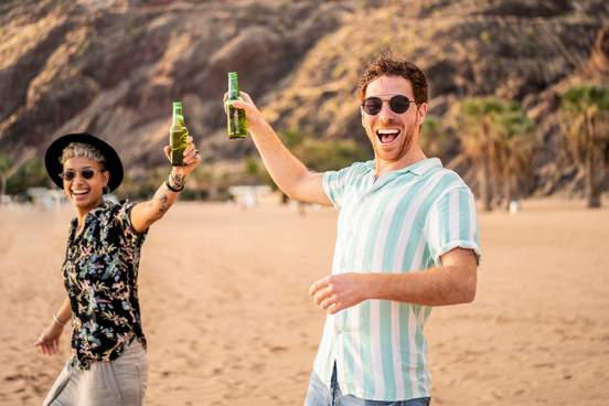 two happy young men drinking beer on beach
