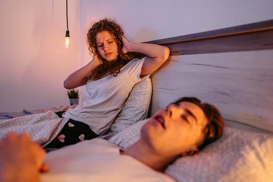 woman covers her ears as boyfriend snores or talks in bed
