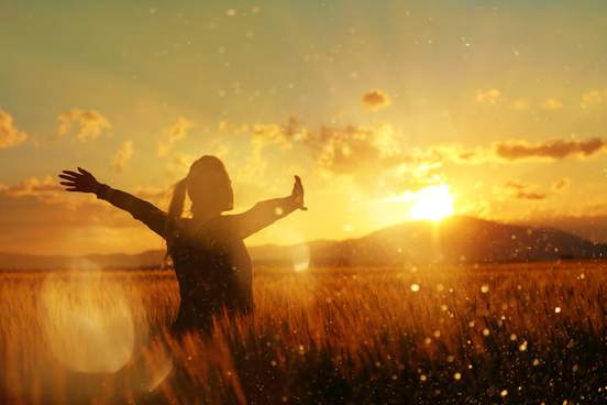 woman standing in a wheat field with sun setting in background