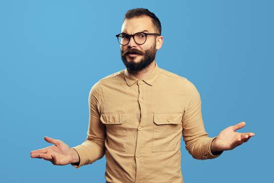 young bearded man in bewilderment shrugging his shoulders and looking at camera with confusion isolated over blue background