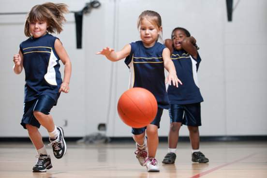 young girls running down a basketball court with a ball