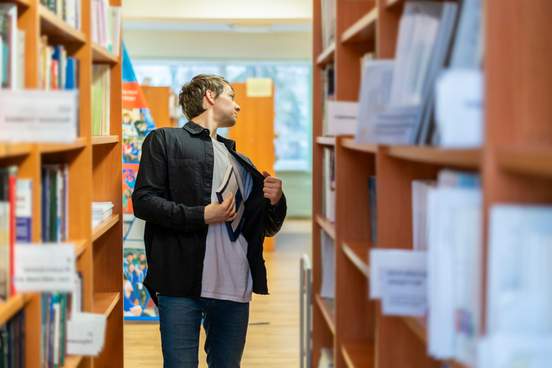 young man stealing a book from library