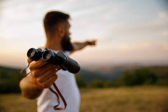young man with binoculars pointing to something in distance
