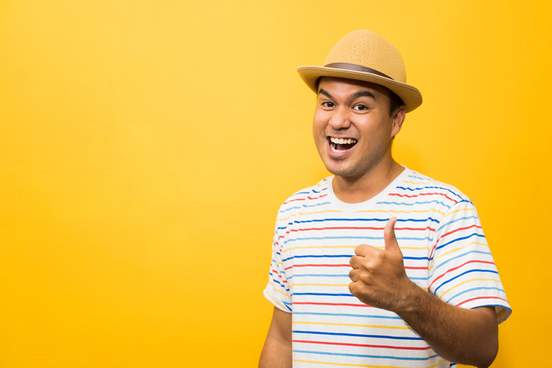 young man with hat feels happy and surprise and showing thumb up on yellow background