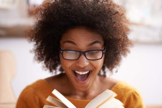 young woman looking delighted as she reads a book