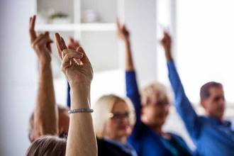 A group of office workers raising their hands while in a meeting