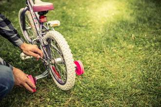 A man's hands adding training wheels to their child's bike