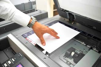 A person's hand placing a piece of paper onto the copy machine