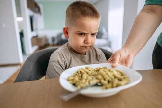 Child looking unhappy at a plate of pasta and refusing to eat