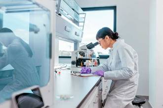 Female scientist looking through a microscope while writing down her observations