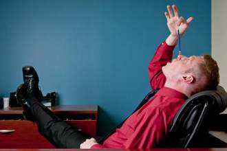 a bored man leaning back in his chair trying to balance a pencil on his nose