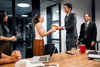 a business man handing a gift to his coworker during an office meeting