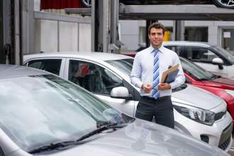 a car salesman looking at the camera standing in front of a car waiting to tell you his spiel
