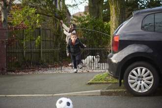 a child who lost his ball is running into the street without looking while his mom is not paying attention in the background
