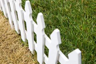 a fence with dead grass on one side and fresh green grass on the other
