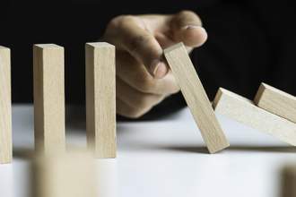 a finger is stopping chain reaction of dominos that is about to fall