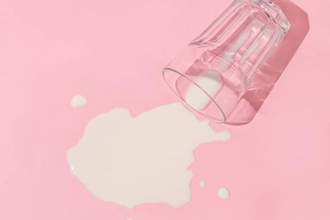 a glass of spilled milk on a light pink background